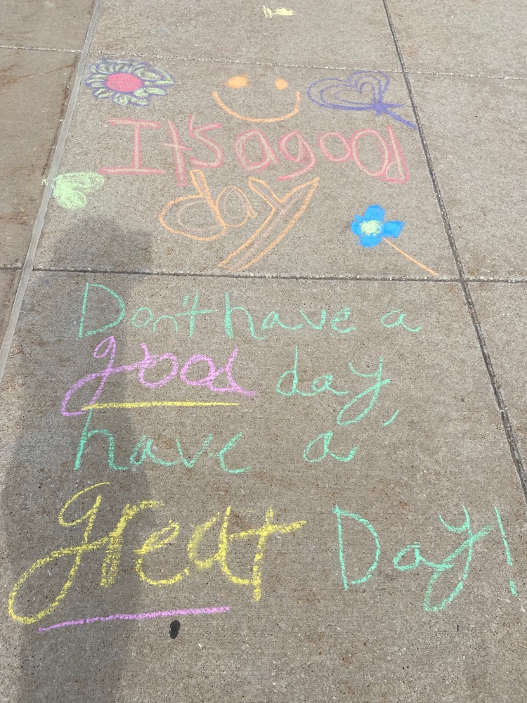 colorful sidewalk chalk on 2 squares, first square says, “it’s a good day” and square under it says, “don’t have a good day, have a GREAT day!"